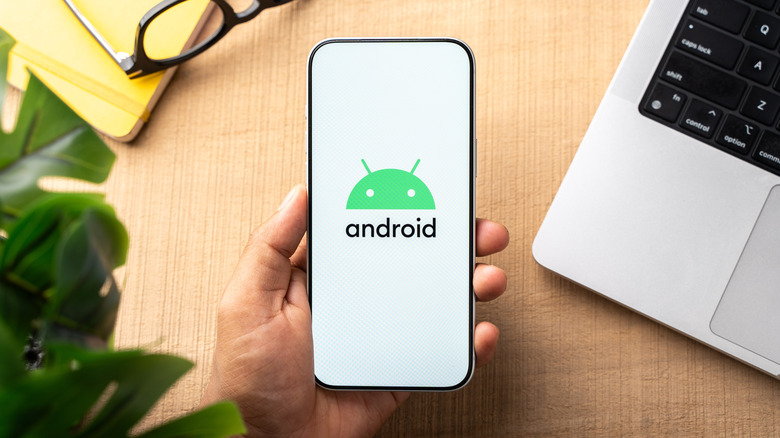 A person holding a smartphone with the Android logo on the screen