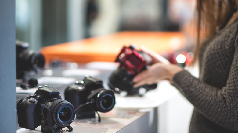 Female customer standing in photographic equipment store and looking at digital camera