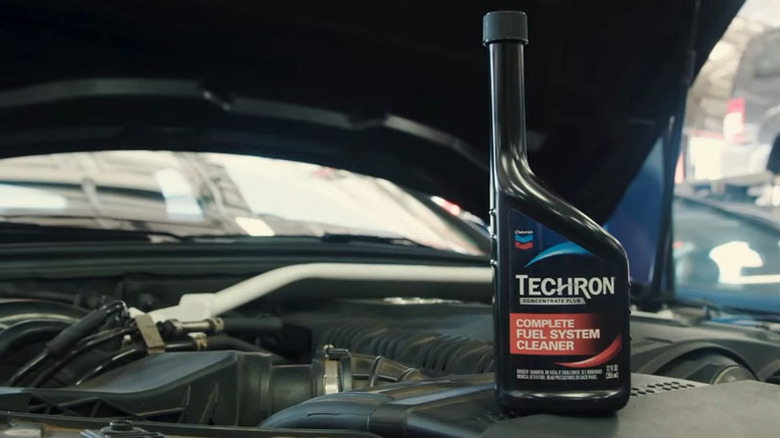 A bottle of fuel system cleaner on the engine of a car with hood open