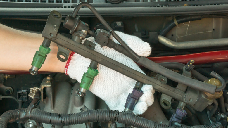 Gloved hand holding a fuel rail with fuel injectors above an engine