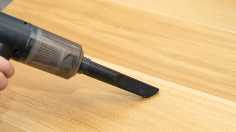 A close-up of a vacuum cleaner's crevice tool cleaning a wood floor