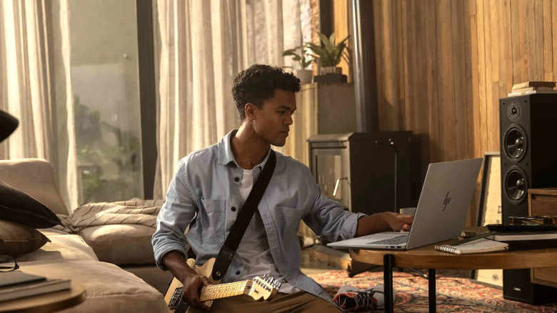 A person using the HP OmniBook 7 with one hand, holding a guitar with the other.
