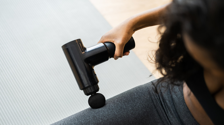 Woman using massage gun on her leg after workout