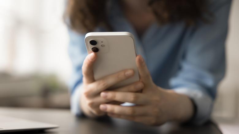 A woman's hands holding a smartphone with her blurred torso in a blue shirt in the background