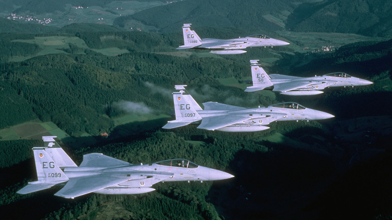 Four F-15 Eagles flying in formation over forests