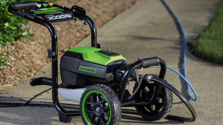 A Greenworks pressure washer sitting on a sidewalk with a hose attached