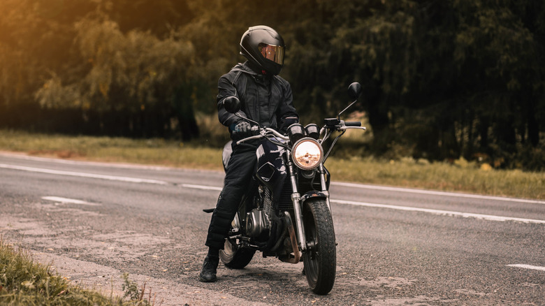 A biker wearing a leather jacket and a helmet on a cafe bike