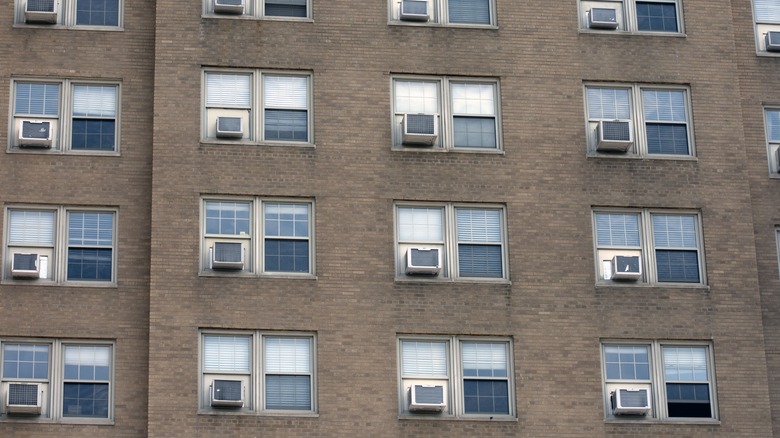 A variety of window air conditioners in a multi-family building seen from the outside.