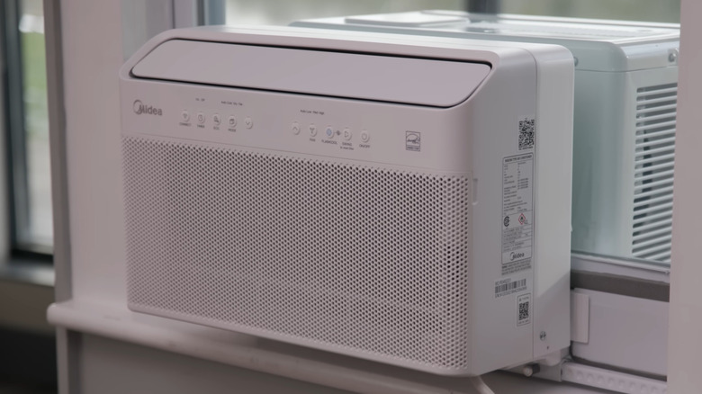 A close-up of the U-shaped Midea window air conditioner on a window, heat pump hiding in the background