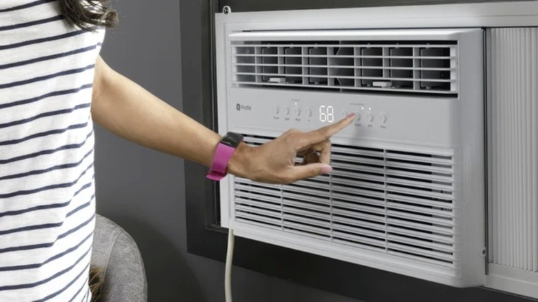 A woman adjusting the front controls of a GE Profile window air conditioner.