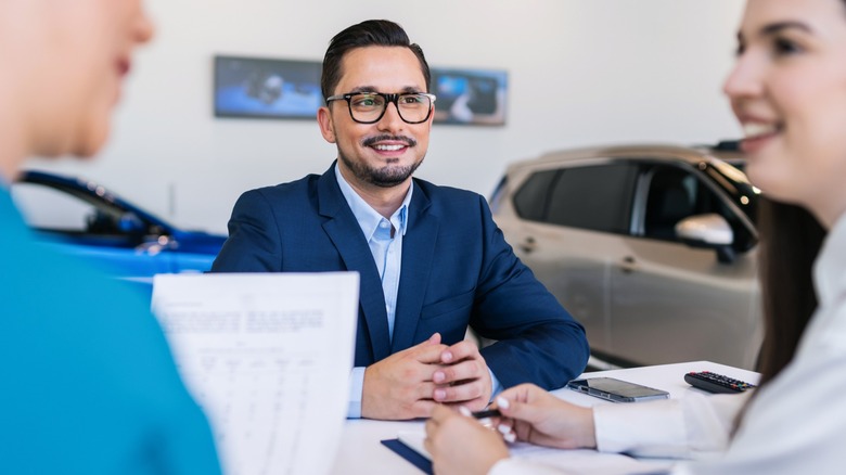 Car dealer is sitting at a table with two customers