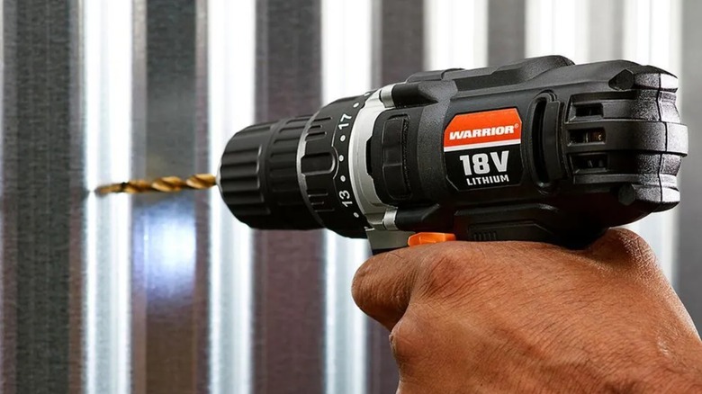 A person using a Warrior drill on metal.