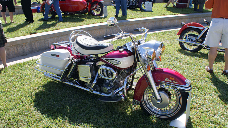 A white and cherry pink FLH Electra Glide on display at a sunny car show