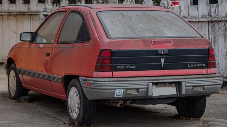 A red Pontiac LeMans parked near a wooden fence