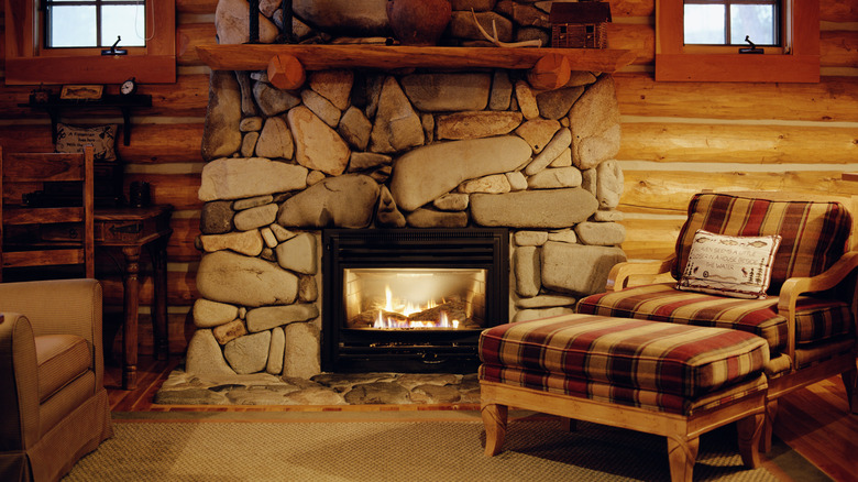 A stone fireplace inside a log home with a cozy chair sitting next to it