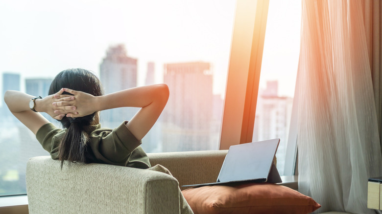 A young woman enjoying the breathtaking views of the city while working on a lpatop whch is placed on a pillow