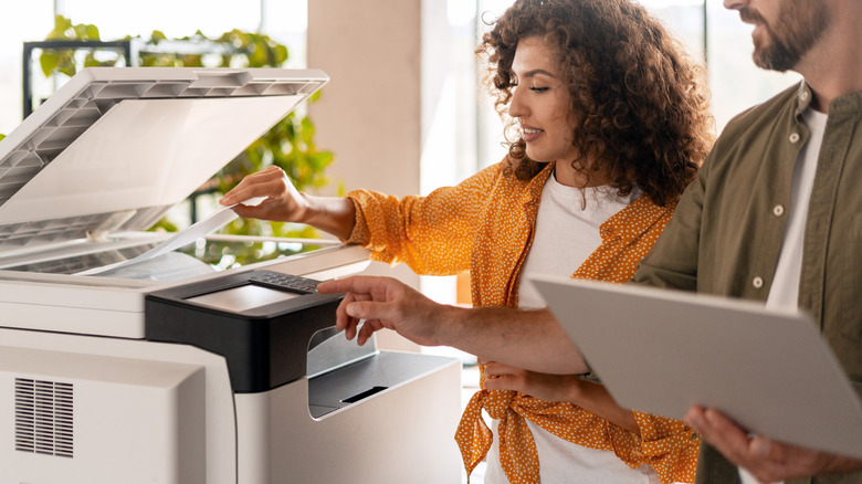 A person putting paper into a printer scanner while someone else uses its console