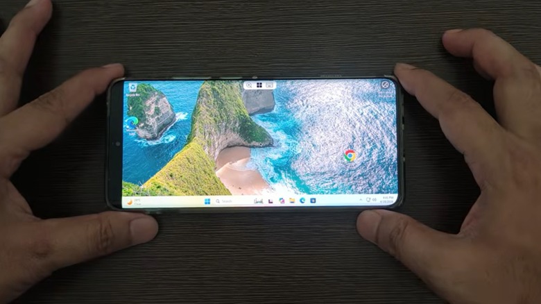 A person holding an Android phone showing a Windows 11 desktop