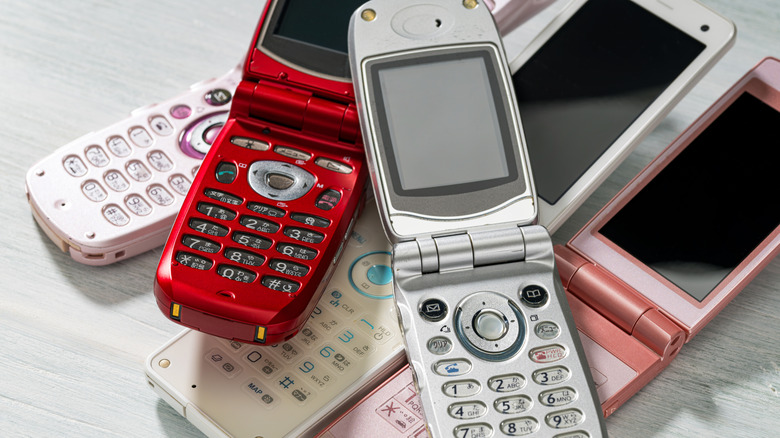 A pile of old flip phones in different colors sitting on a light surface