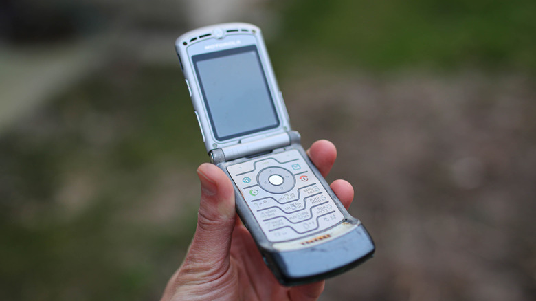 A hand holding up a Motorola Razr V3 flip phone