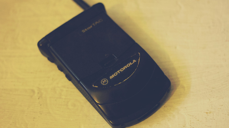 A black Motorola StarTAC flip phone sitting closed on a wood surface
