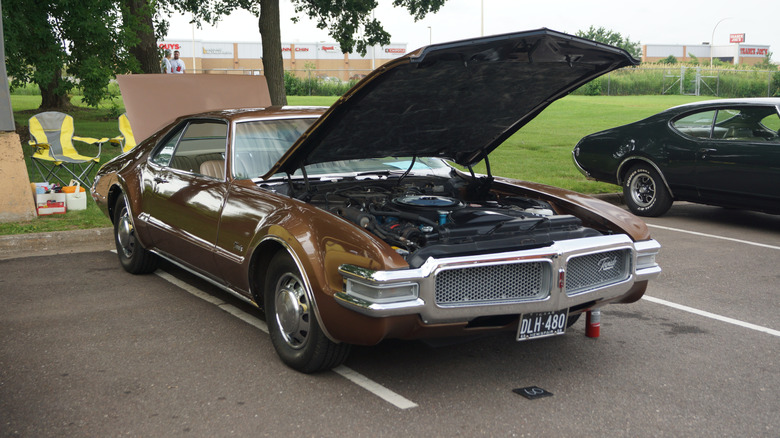 A brown 1968 Oldsmobile Toronado on a parking lot with the hood open, front 3/4 view