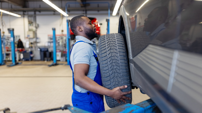Male mechanic removing car wheel of lifted automobile