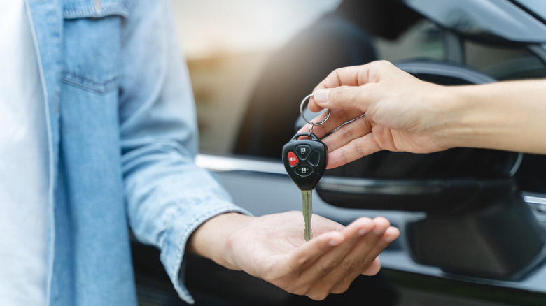 Close-up of one hand setting car keys into someone else's palm with a black vehicle in the background