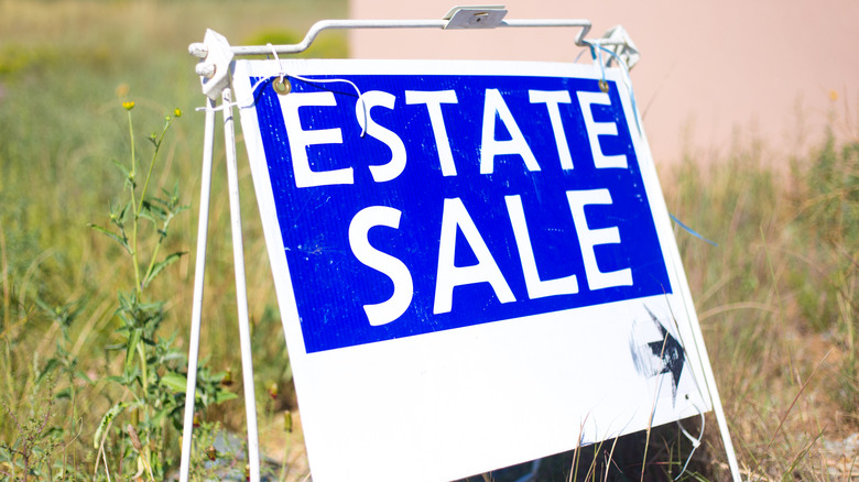 A large blue sign on grass advertising an estate sale
