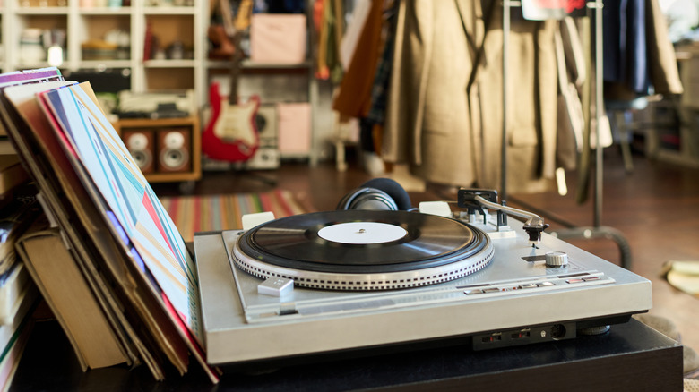 An old turntable with vinyl records in a thrift store with coats and other items in the background