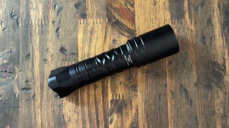 A Malkoff MD2 flashlight on a wooden surface.