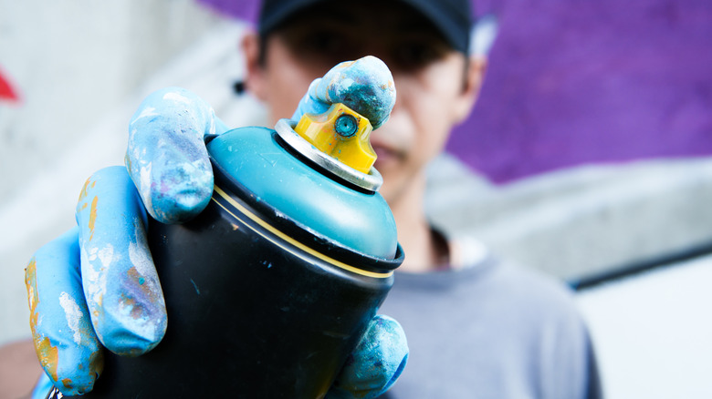 Person pointing a spray paint can directly at the camera