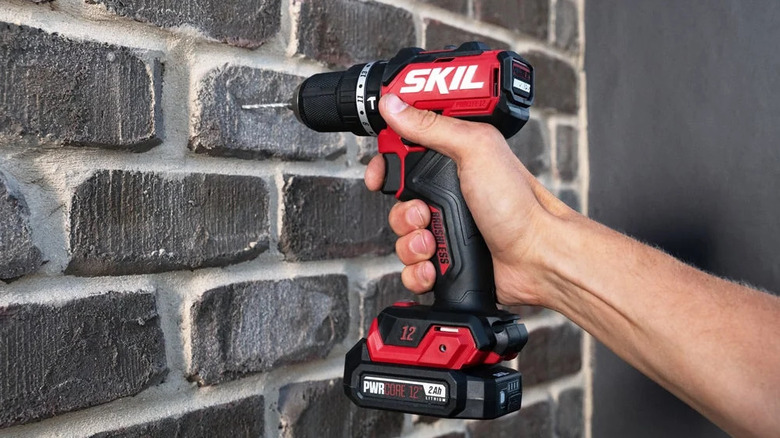 close-up of a person using a Skil 12V brushless half-inch hammer drill on a brick wall