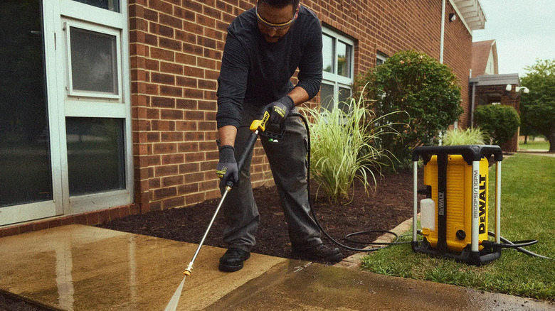 A man using a DeWalt 2600 PSI 1.1 GPM Electric Jobsite Pressure Washer to clean a home's front walkway
