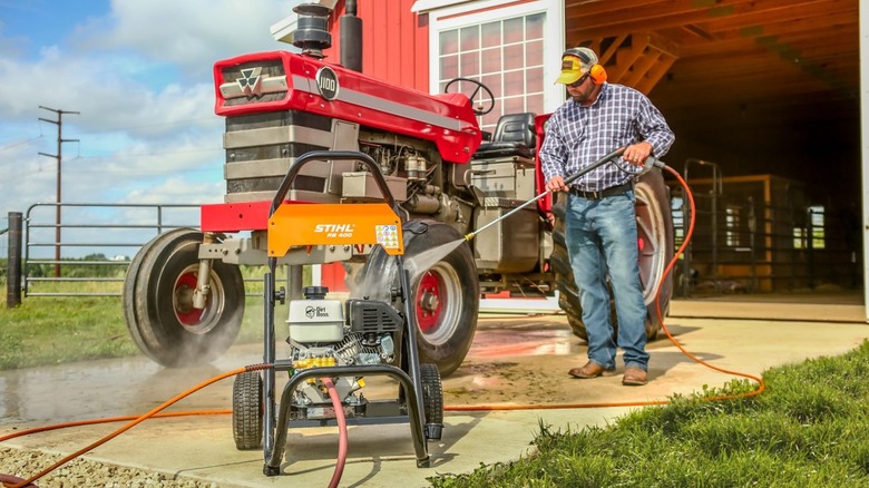 A man using a Stihl RB 400 Dirt Boss pressure washer to clean a tractor in front of a barn