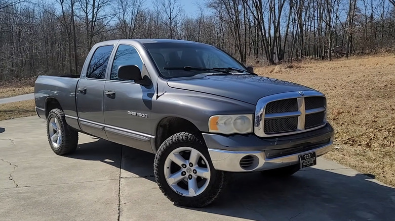 A gray 2002 Ram 1500 parked on road, trees in the background.