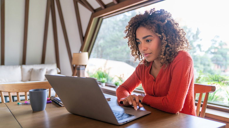 A person sitting with their back to the window using a laptop.