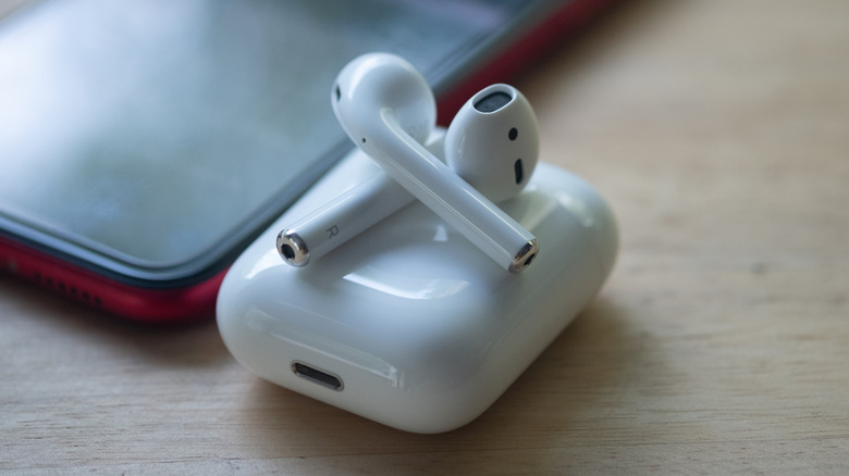 AirPods on their charging case beside a phone.