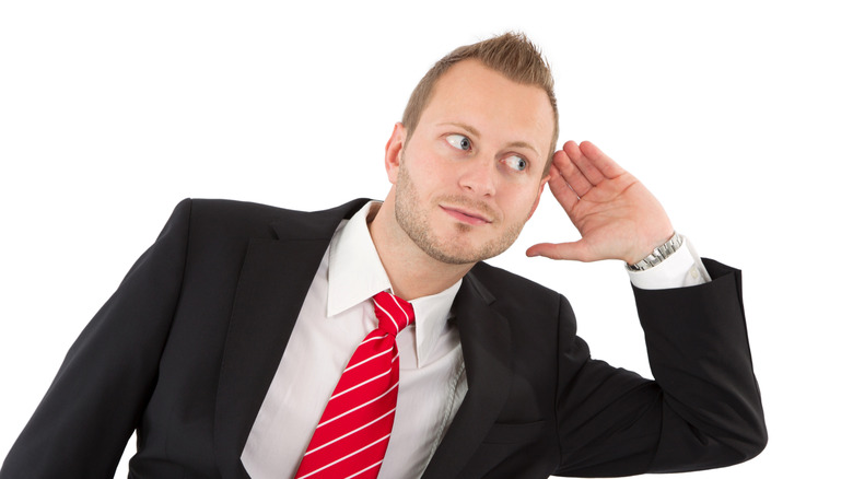 A man in a suit trying to listen to something more intently with his hand cupped over his ear