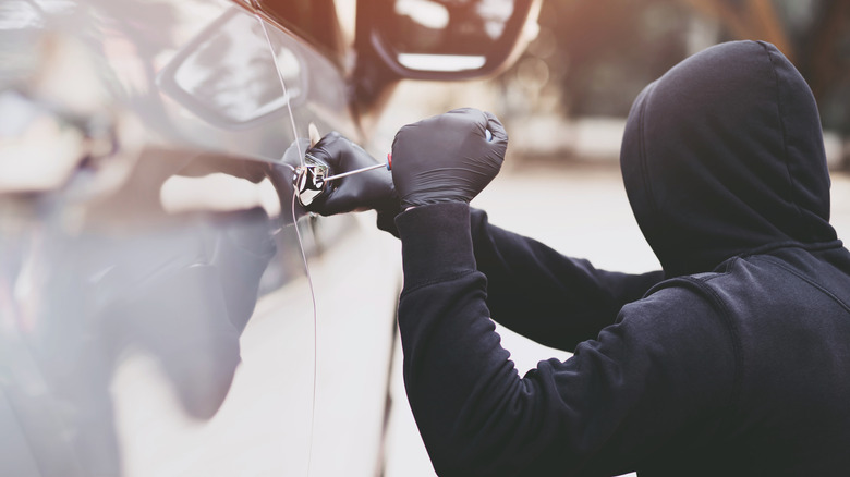 hooded man trying to break into silver car