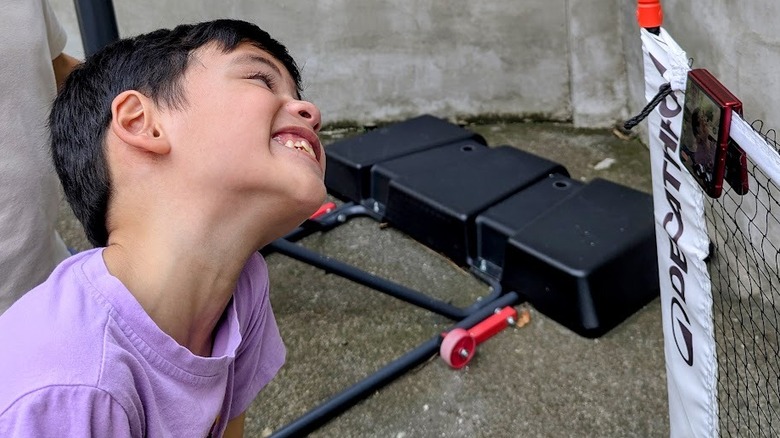 A child smiling at a phone camera hanging from a pickleball net