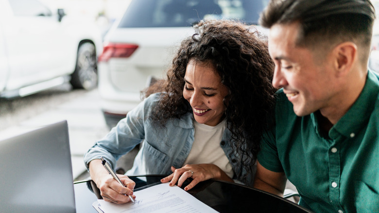 A smiling couple signing paperwork inside a car dealership