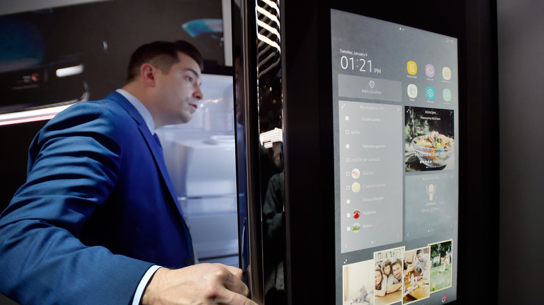 A man in a blue suit looking curious as he opens a Samsung refrigerator with a built-in smart screen