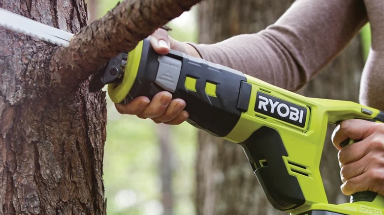 A person using a Ryobi reciprocating saw on a branch.