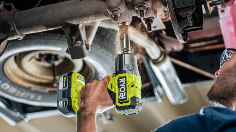Person using Ryobi cordless impact wrench on underside of car