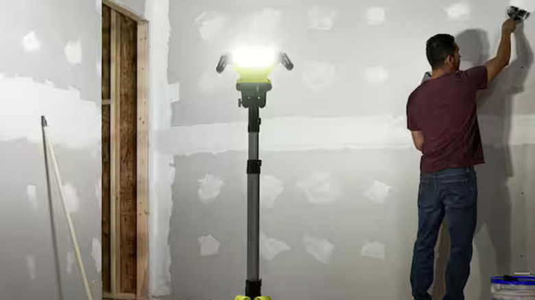 A man working on drywall with the assistance of a Ryobi tripod light