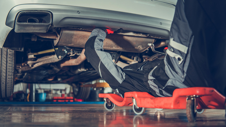 A person working on the exhaust system of a car while sitting in a creeper chair