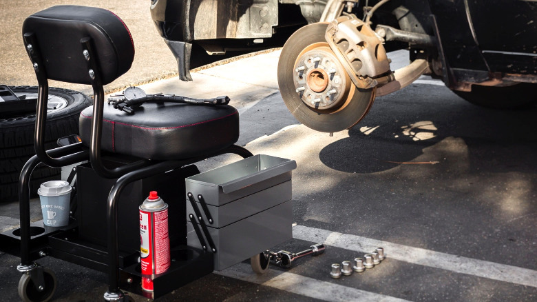 The Powerbuilt Shop Seat With Expandable Side Trays in front of a car.