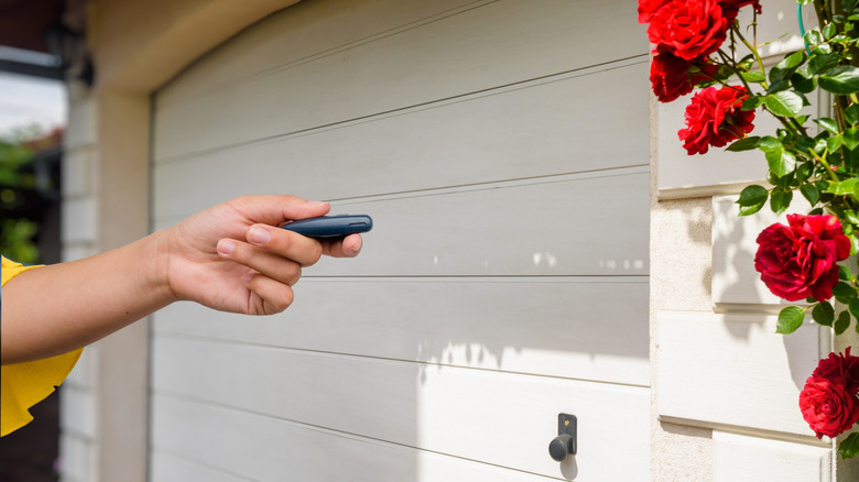 Hand pressing button on garage door opener with unresponsive garage door in background.