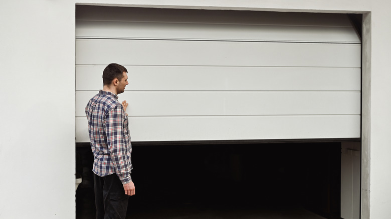 Man standing near garage door as if monitoring it as it opens or closes.